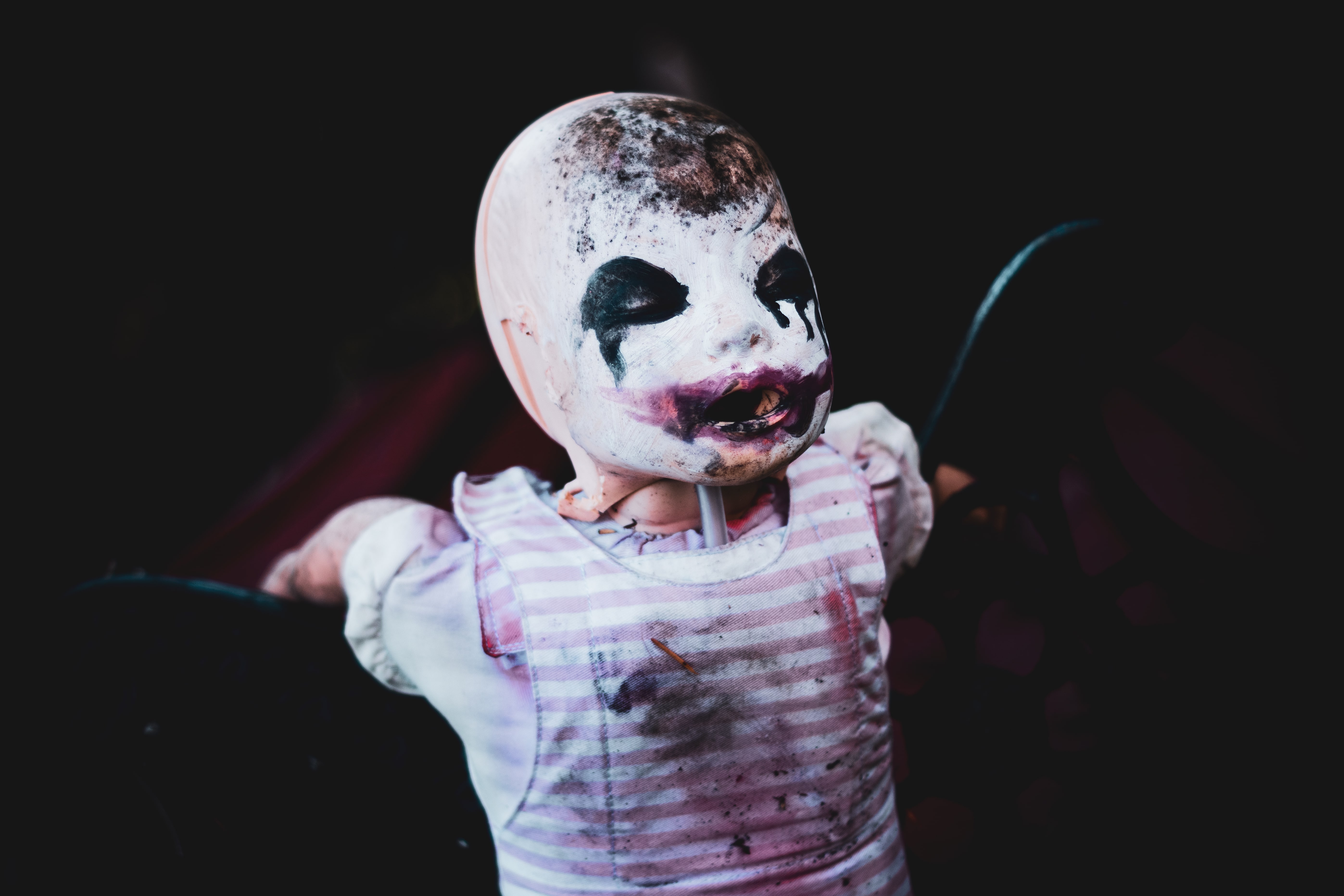 A photo of an abandoned baby doll whose face is covered in melting and smudged clown makeup. 
