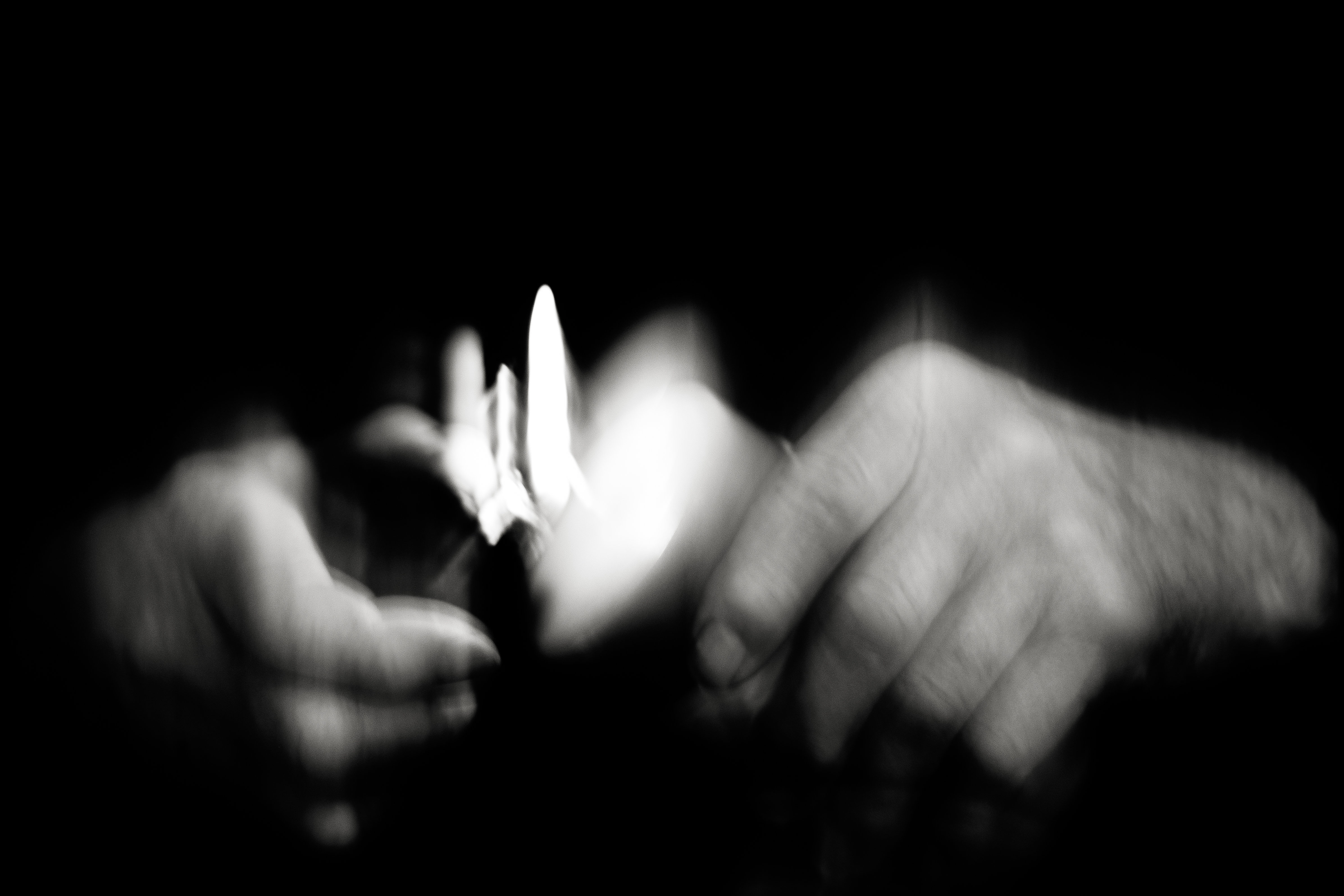 A blurry artistic photo, in black and white, of two hands holding a lighter and setting fire to some paper.